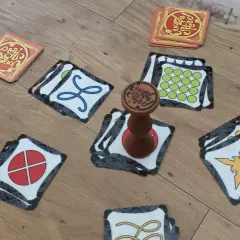 Karty gry Jungle Speed rozłożone na podłodze, gotowe do szybkiej rozgrywki. Drewniany totem pośrodku.