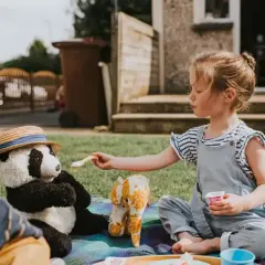 Dziewczynka karmi pluszową pandę w kapeluszu. Zabawa w piknik to świetna okazja do rozwiązywania krótkich zagadek.