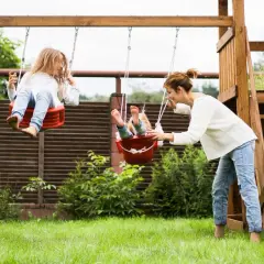 Mama pcha huśtawki, na których bawią się dzieci. Radosne zabawy dla dzieci na placu zabaw.
