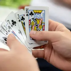 Ręce trzymają karty do gry: Król trefl, Walet trefl, 7 trefl, 6 pik, 8 karo. Czy to początek gry oszust?