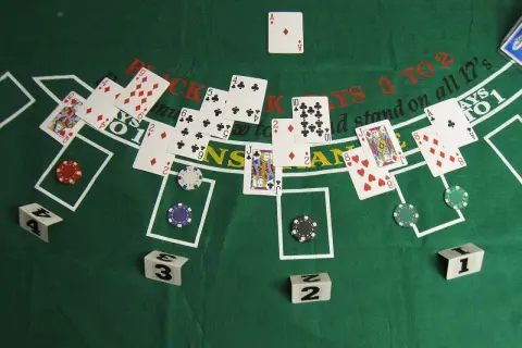 Stół do gry w blackjacka, karty i żetony. Widać karty z królem, damą i asem. Gra 21 w toku.