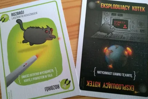 Karty z gry "Eksplodujące Kotki". Jedna pokazuje kota celującego laserem w rakietę, druga to instrukcja z kotem przy panelu kontrolnym i Ziemią w płomieniach.