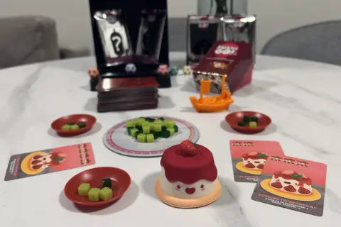 Gra Sushi Go Party! z uroczym puddingiem truskawkowym i kostkami do gry.