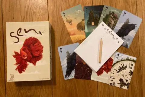 Pudełko gry karcianej "Sen" i rozłożone karty z surrealistycznymi ilustracjami, jak latające wyspy i mroczne zamki.