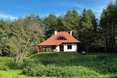 Urokliwy domek na wzgórzu pośród baśniowego boru. Otoczony zielenią, z czerwoną, spadzistą dachem i werandą.