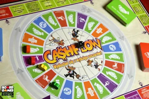 Gra w szczury na planszy Cashflow. Myszy w garniturach biegną po okręgu, rzucając kostką.