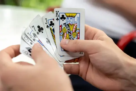 Ręce trzymają karty do gry: Król trefl, Walet trefl, 7 trefl, 6 pik, 8 karo. Czy to początek gry oszust?