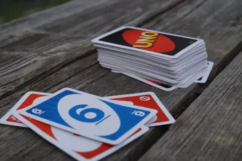 Karty UNO leżą na drewnianym stole. Jedna szóstka niebieska i dwie czerwone. Stos kart z logo UNO czeka na kolejnego gracza.
