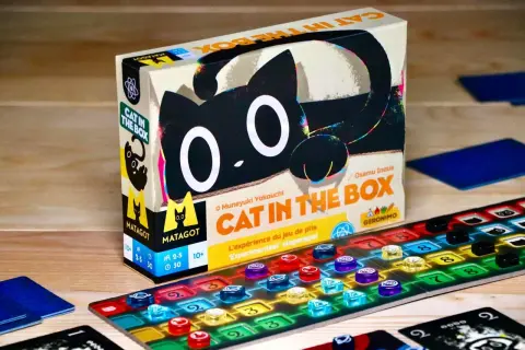 Gra planszowa "Cat in the Box" z czarnym kotem na pudełku i kolorowymi znacznikami na planszy.