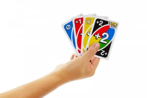 Ręka trzyma karty: niebieską z symbolem, czerwoną +1, żółtą ze strzałką i czarną z napisem UNO FLIP! oraz +2.